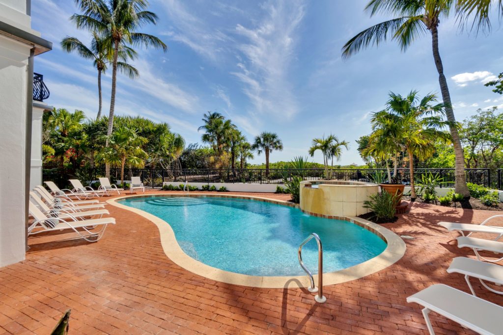 A pool with blue water near palm trees and white beach chairs and a fountain at the Sea Oats Estate in Captiva Island, FL