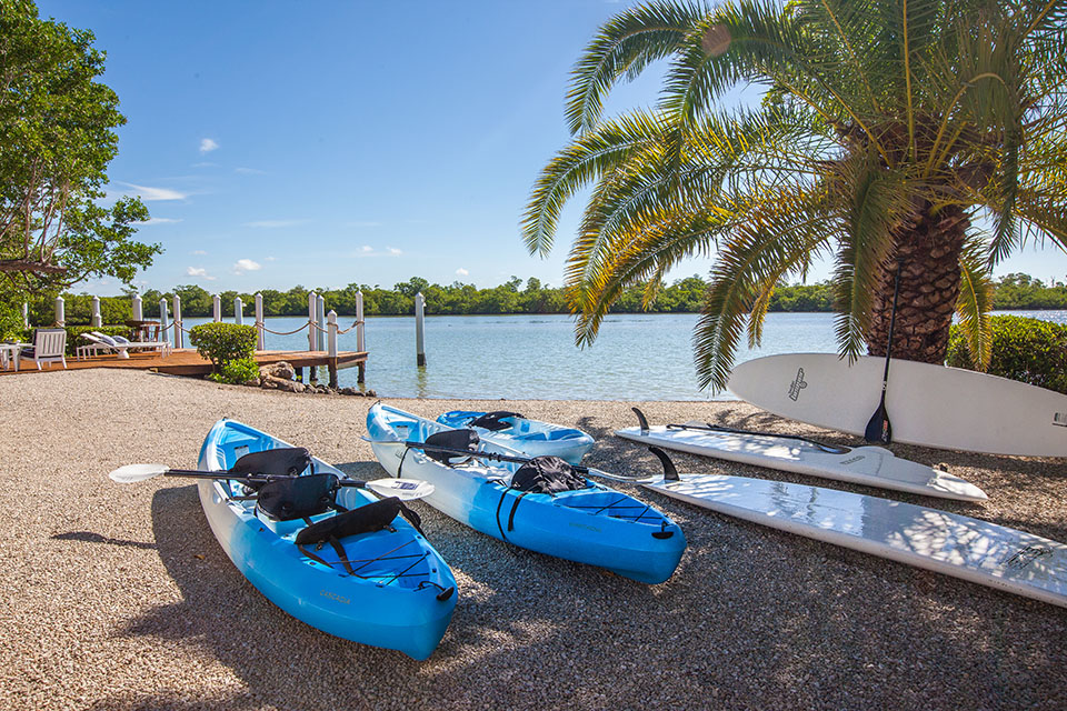 Two blue kayaks and white paddle boards on the shore of the beach next to a wooden dock in Captiva Island, FL