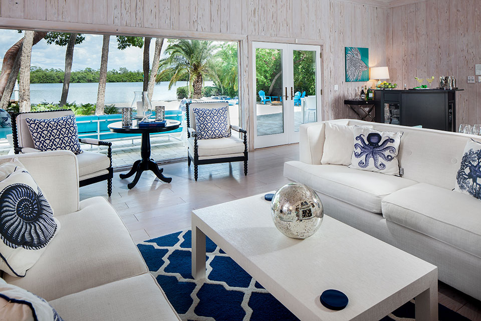 Living room in Sea Oats Estate with white couches and white coffee table with a navy blue and white rug underneath, a view of the pool area and ocean with wood plank walls and a bar area