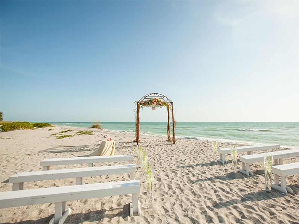 Wedding ceremony setup on the beach of Captiva Island, FL with white benches and a wooden arbor