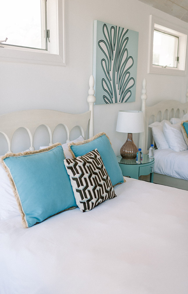 Bedroom in the Sea Oats Estate with two queen beds, with white linen sheets, two blue and one black and white decorative pillows, a blue circular night stand white and white and brown glass lamp in Captiva Island, FL