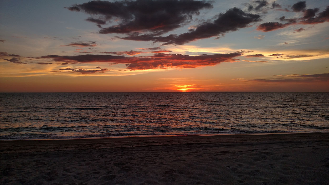 A sandy beach with a sun setting in the background with clouds in the sky at the Sea Oats Estate in Captiva Island, FL
