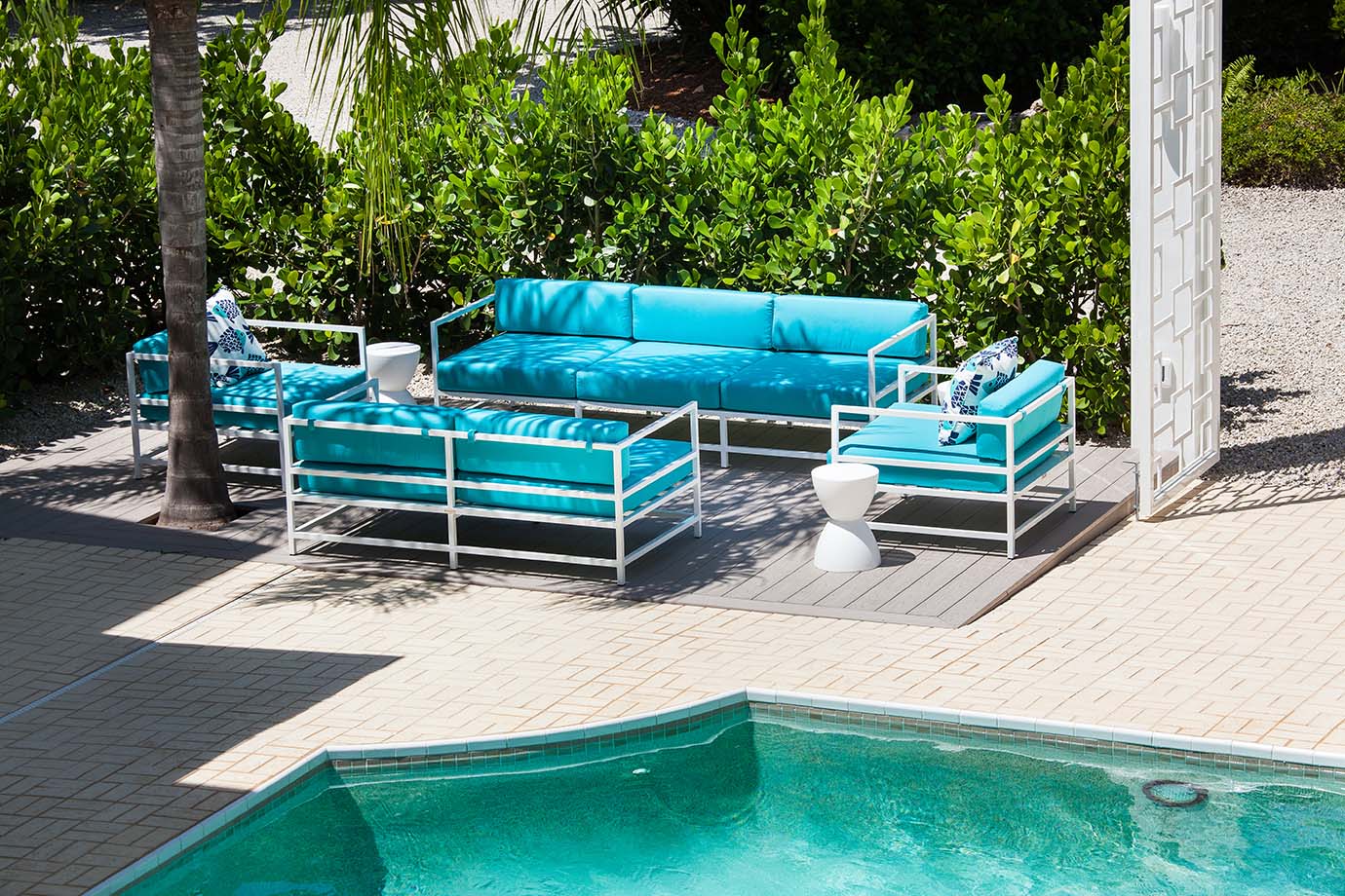 Bright blue inground pool with a blue and white lounge furniture set off the side surrounded by green bushes at the Sea Oats Estate in Captiva Island, FL