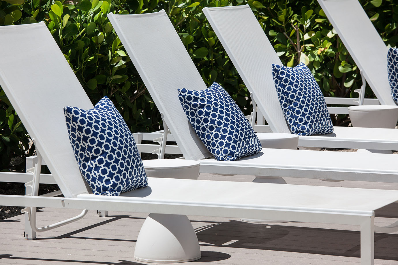 Row of white pool chairs with small circular side tables and navy blue and white pillows at Sea Oats Estate