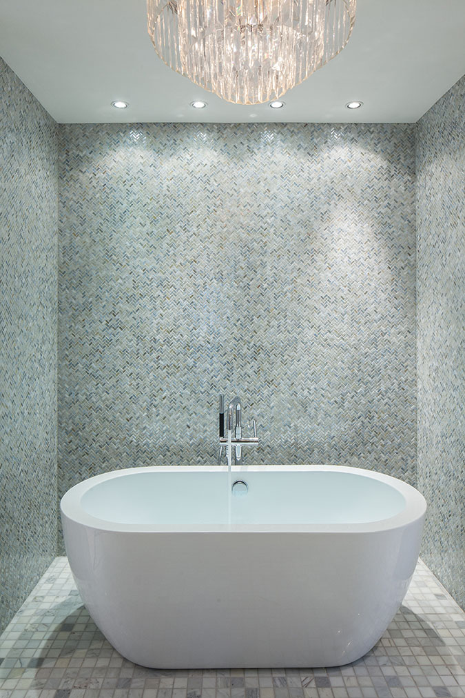 White soaking tub in the Sea Oats Estate in Captiva Island, FL surrounded by tiled walls and a crystal chandelier