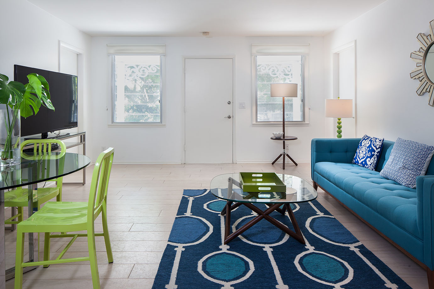 Guest house entrance way, with a blue fabric couch, a nay blue carpet with circular patterns, a coffee table a glass top, a glass table with lime green metal chairs and a tv stand with a large flat screen tv in Captiva Island, FL