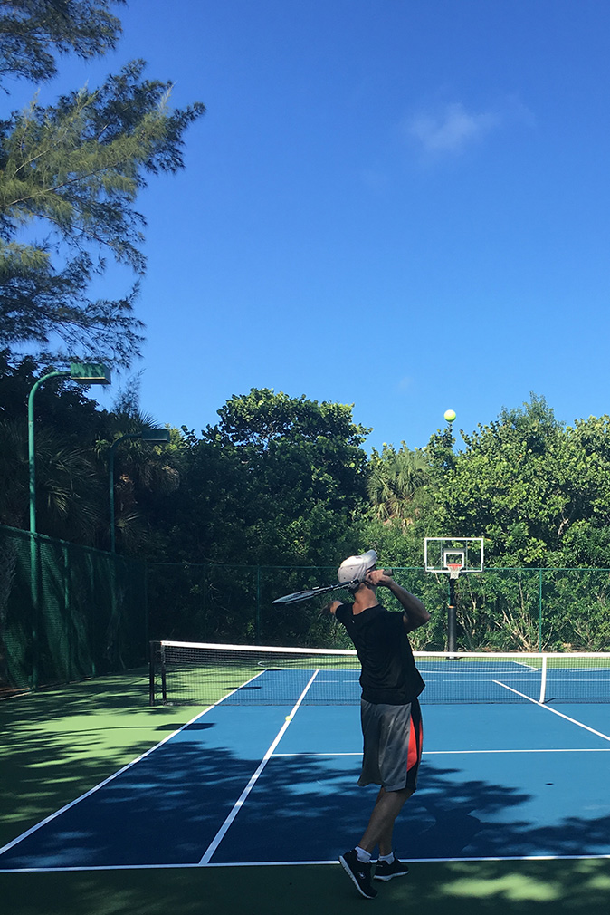 Man playing tennis on the Sea Oats Estate courts surrounded by green plants and trees