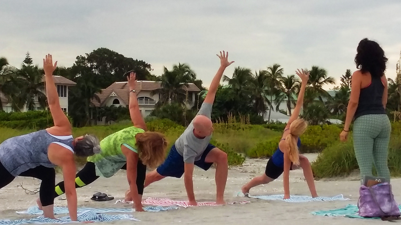 Group of people doing yoga on the beach with an instructor with view of the other houses in Captiva Island, FL in the background