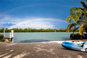 View of the private beach with blue and white kayaks, a private dock with a rainbow over the ocean in Captiva Island, FL