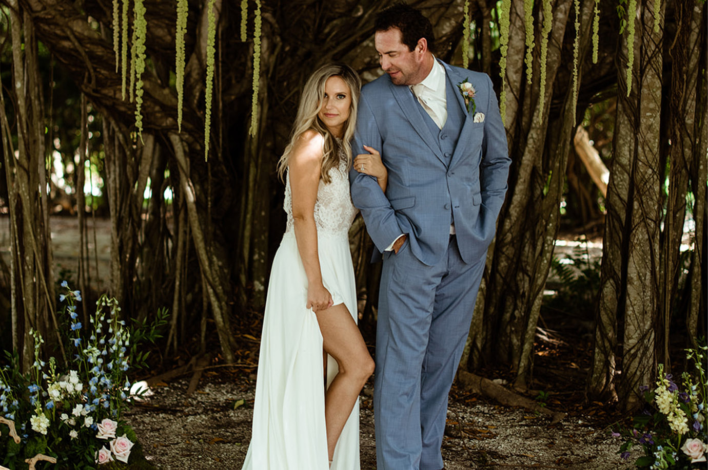 Bride and groom standing under an overgrown tree looking at each other with greenery dangling from the branches and florals surrounding in Captiva Island, FL