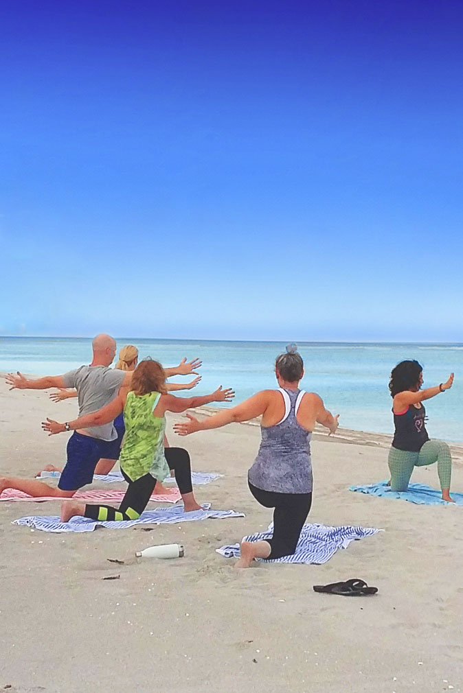 A group of people doing yoga on a sandy beach with clear blue skies at the Sea Oats Estate in Captiva Island, FL