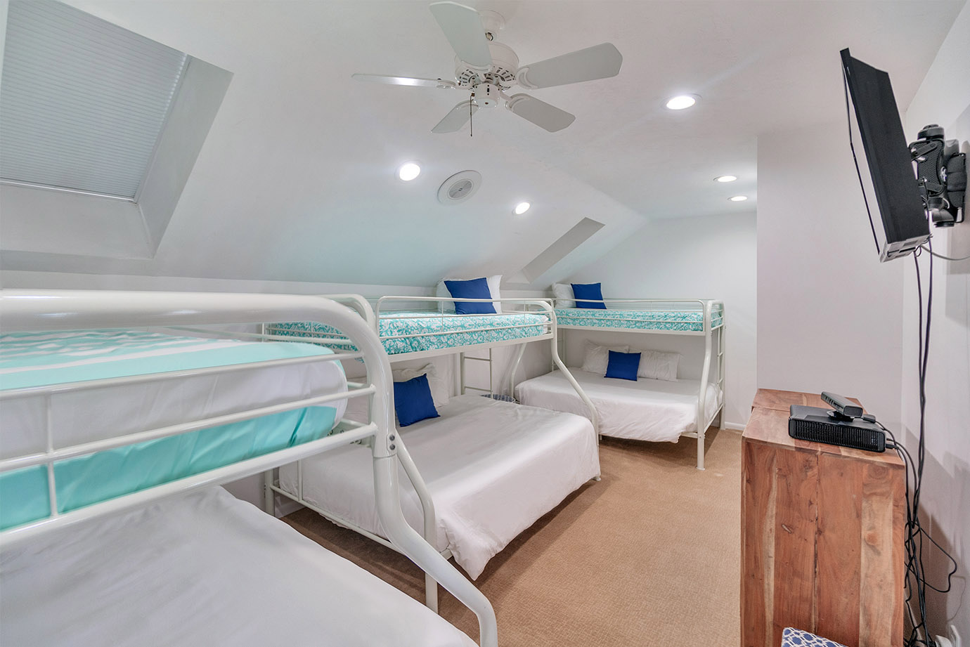 Bedroom in the Sea Oats Estate in Captiva Island with three bunk beds white white and blue linens with a wooden dresser and television on the wall