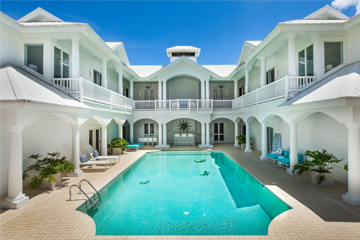 Pool with clear water outside large, white estate with balconies and poolside chairs and plants at the Sea Oats Estate in Captiva Island, FL