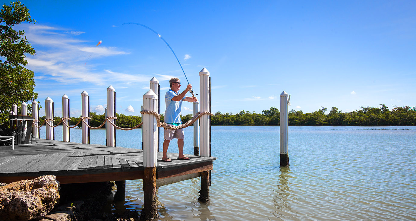 Man fishing off the end of the dock casting a fishing pole into the ocean in Captiva Island, FL