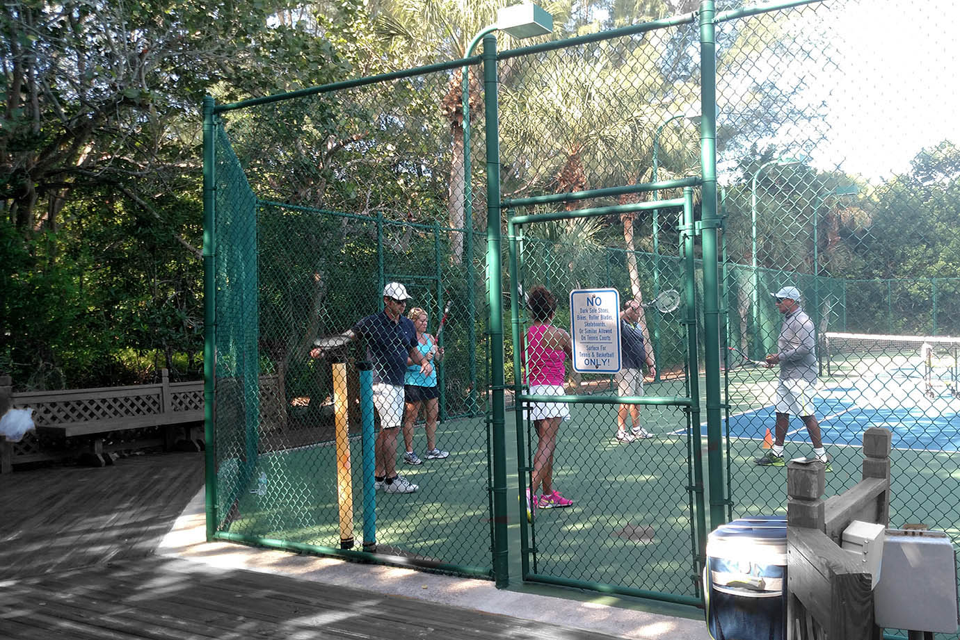 Group of people inside outdoor tennis court with fence near trees at the Sea Oats Estate in Captiva Island, FL