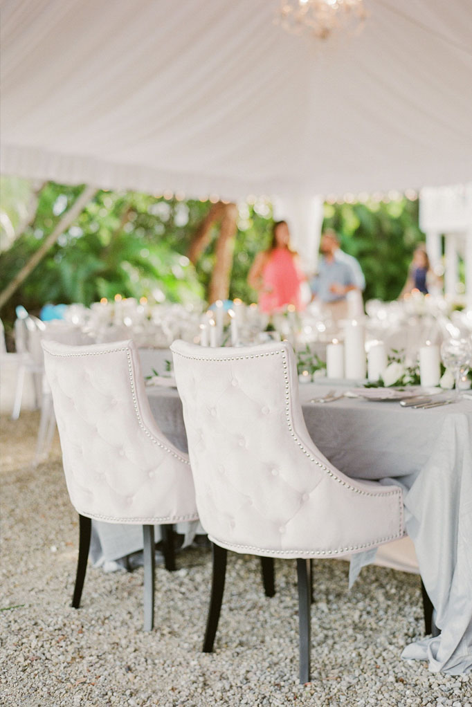 Bride and groom head table with a gray linen set for dinner service with white candles and white upholstered chairs at Sea Oats Estate