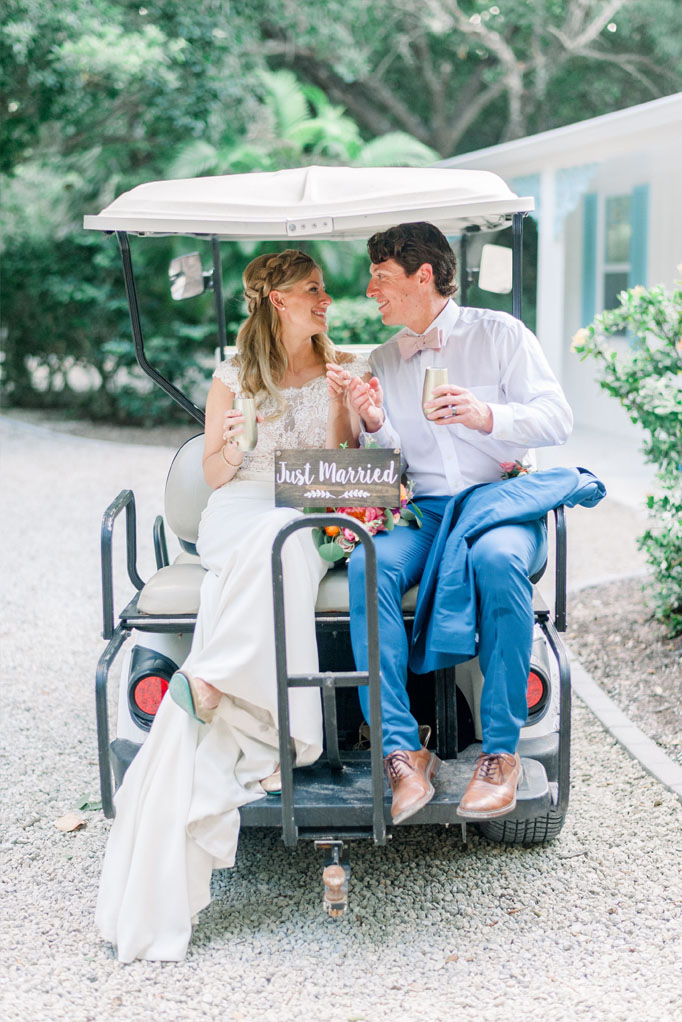 Bride and Groom on the back of a golf cart, holding a just married sign and champagne glasses at the Sea Oats Estate in Captiva Island, FL