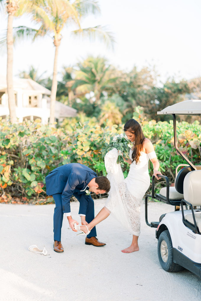 Bride and groom getting off a golf cart with the bride holding her white dress as the groom puts on her shoes in Captiva Island, FL