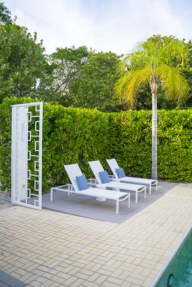 Three white lounge chairs by the pool surrounded by a plant wall surrounded by palm trees at the Sea Oats Estate in Captiva Island, FL