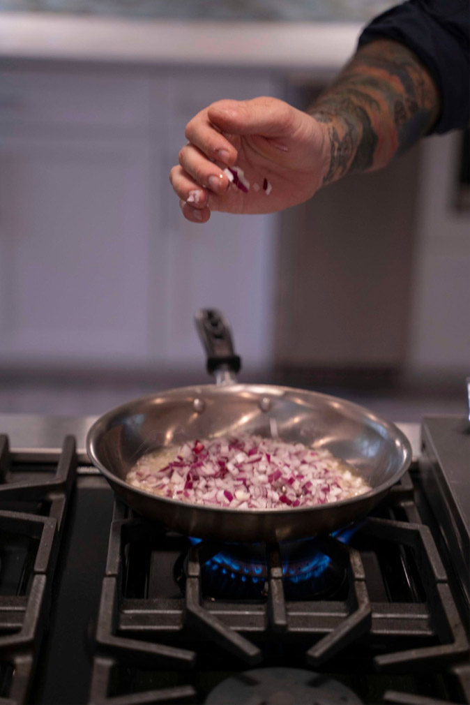 Chef at the Sea Oats Estate in Captiva Island, FL sauteing red onion in a stainless steel pan