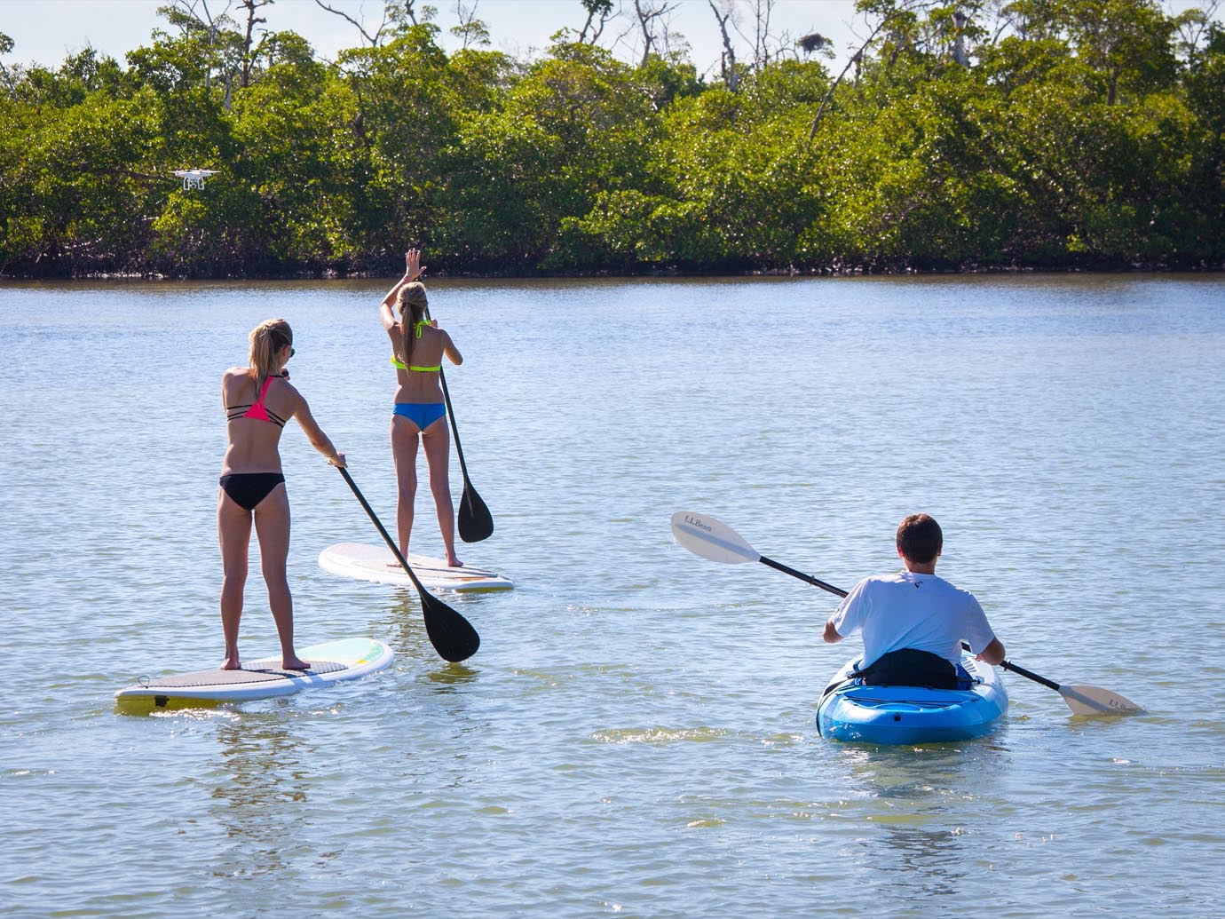 Two woman on paddle boards and a man in a blue kayak moving along through the ocean inlet in Captiva Island, FL