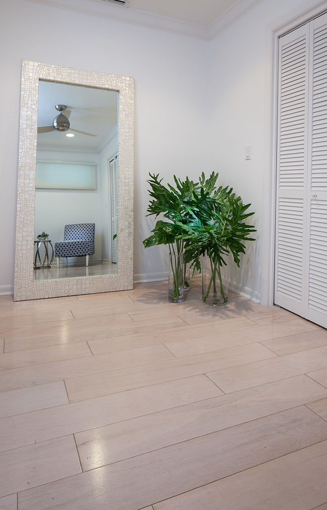 Part of a bedroom in the Sea Oats Estate with a large full length mirror with oversized greenery in clear large vases