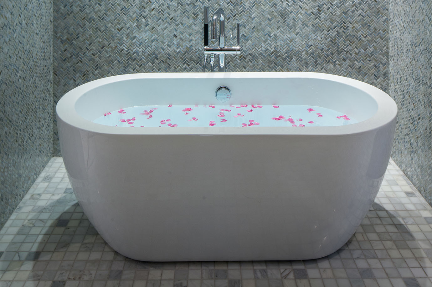 White soaking tub in the Sea Oats Estate filled with water and rose petals, surrounded by tiled walls in Captiva Island, FL