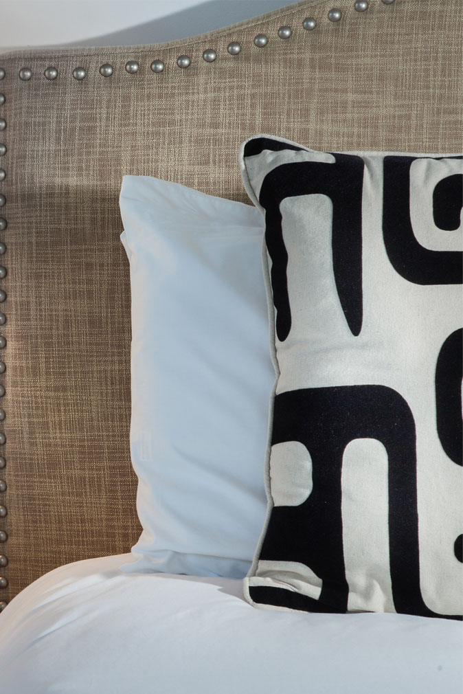 White pillow and a decorative pillow with a black and white pattern in front of a headboard on a bed with white linens at the Sea Oats Estate in Captiva Island, FL