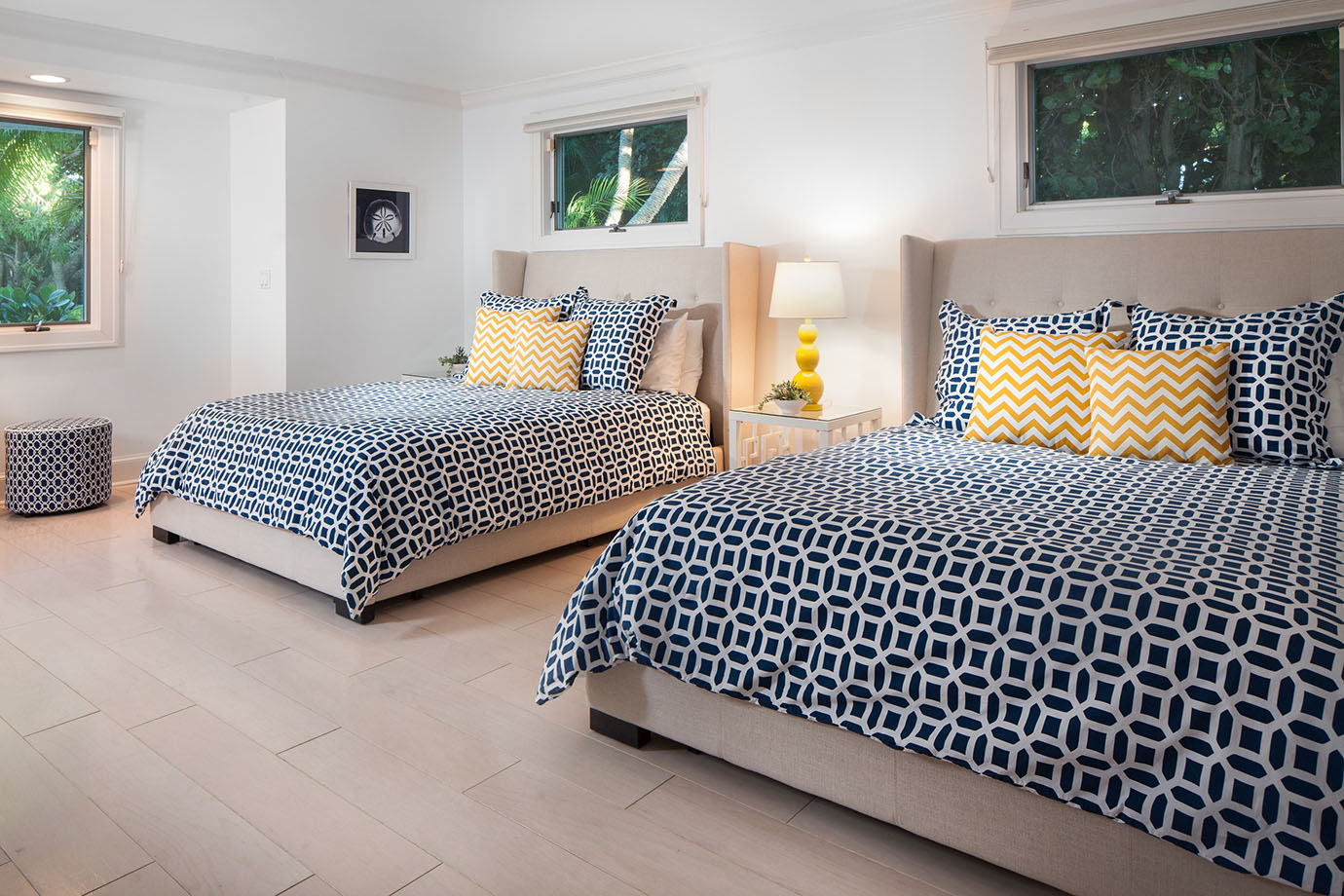 Two queen beds with decorative black and white pattern with white and yellow pillows next to bedside table and lamp at the Sea Oats Estate in Captiva Island, FL