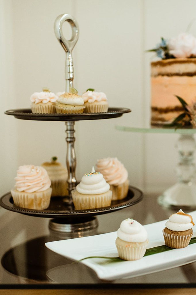 Array of cupcakes displayed on platters on a clear glass top table with a floral arrangement at the Sea Oats Estate in Captiva Island, FL