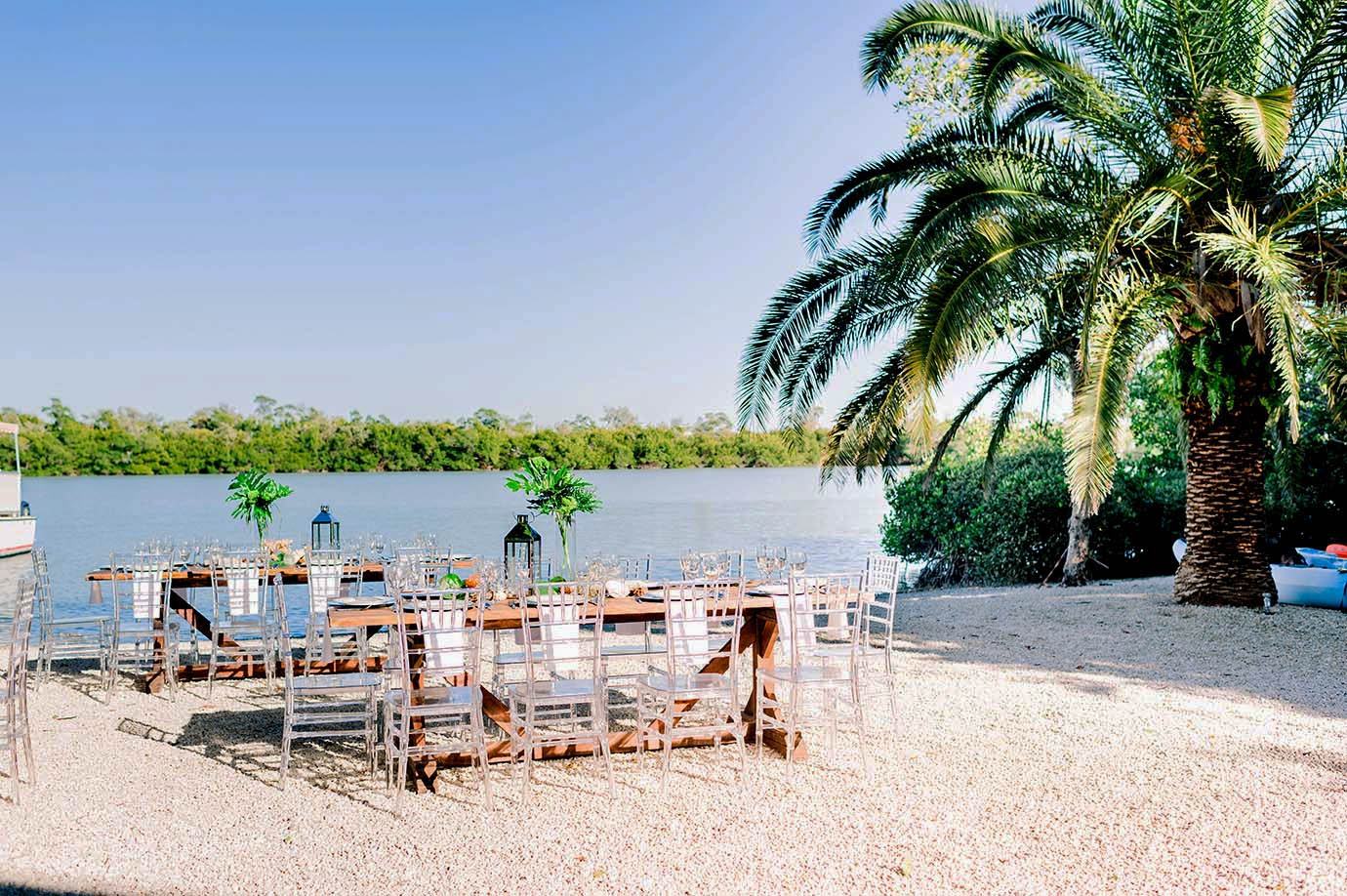Tables and Chairs on beach overlooking the ocean near boat and palm trees at the Sea Oats Estate in Captiva Island, FL
