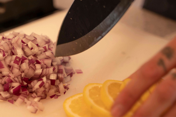 Chef chopping onions and lemon with a knife on a white cutting board at Sea Oats Estate